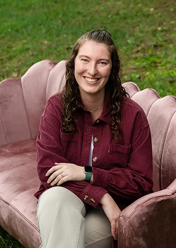 Rachel McMartin sits with one arm crossed over her other on her lap, smiling at the camera.